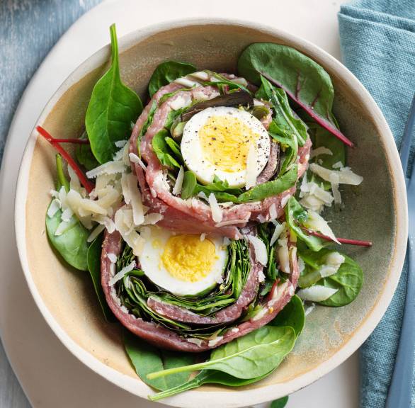 Zwei Rinderfilet-Carpaccio-Roulade gefüllt mit halbierten Eiern angerichtet auf Salatbetten auf zwei Tellern