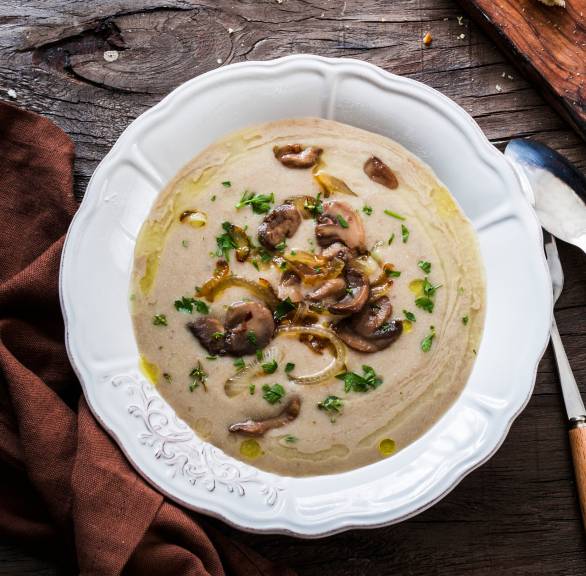 Selbst gekochte Champignoncremesuppe in einem Suppenteller garniert mit Pilzscheiben und Zwiebeln, daneben Ciabatta