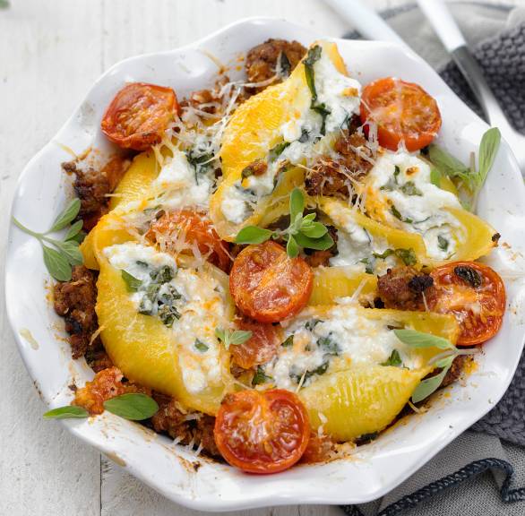 Gebackene Conchiglioni mit Ricotta-Füllung auf Hackfleischsoße in einer Auflaufform auf einem Tisch