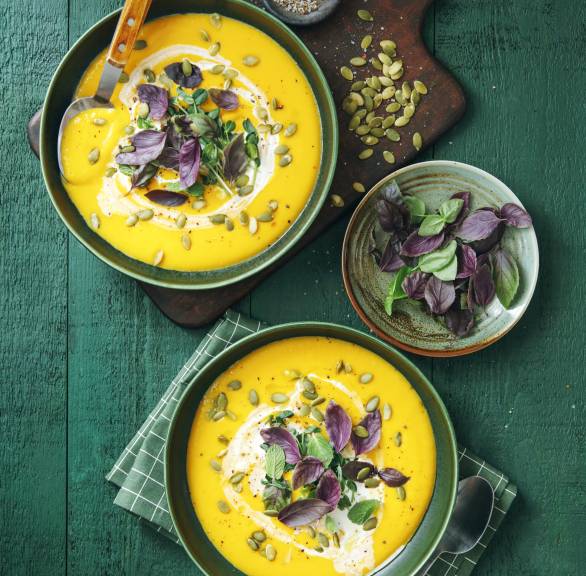 Kürbissuppe in zwei Suppenschüsseln auf einem Tisch getoppt mit frischen Kräutern und Kürbiskernen