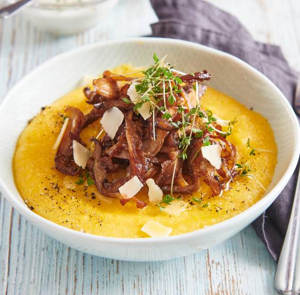 Polenta in einem tiefen Teller getoppt von gebratenen Austernpilzen und Parmesanspänen