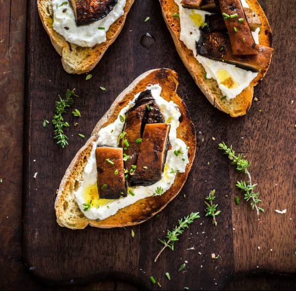 Drei Crostini mit Ricotta und gebratenen Steinpilzen auf einem Holzbrett