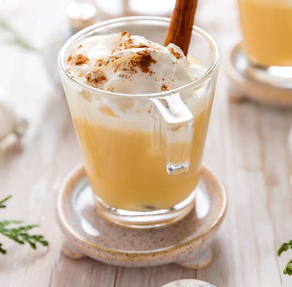 Selbst gemachter Eierpunsch in mehreren Gläsern getoppt mit Gewürzsahne auf einem Tisch