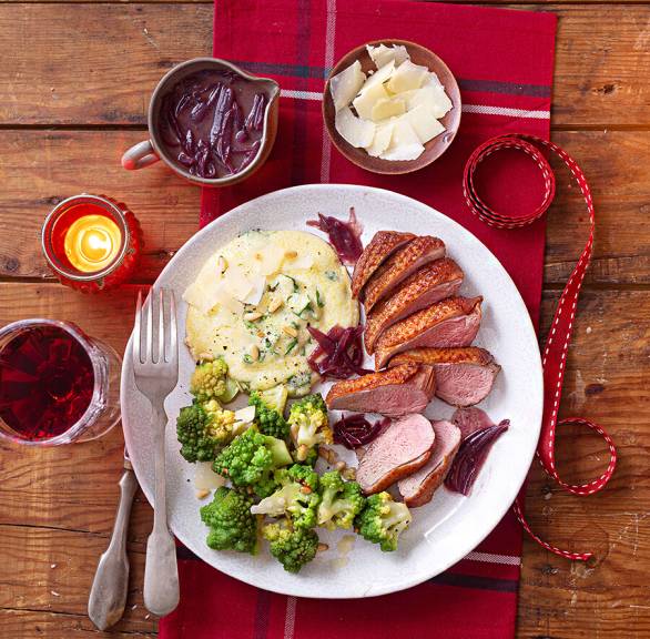 Entenbrust in Scheiben auf einem Teller, daneben mit Romanesco und Polenta auf einem festlich dekorierten Tisch