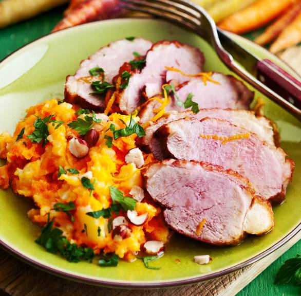 Entenbrustfilet mit Karottenstampf auf einem Teller, daneben Mandeln und Karotten auf eine Tisch