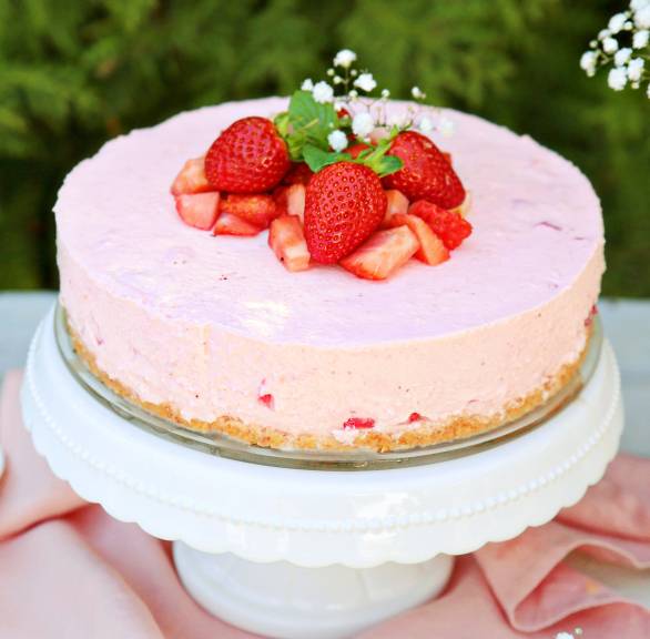 Erdbeer-Joghurt-Torte dekoriert mit frischen Erdbeeren auf einer Tortenplatte im Garten