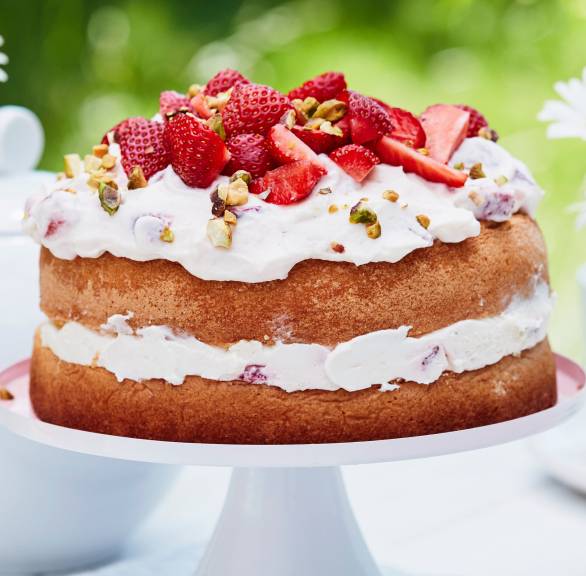 Mehrstöckige Erdbeer-Sahne-Torte mit einem Topping aus frischen Erdbeeren und Pistazien auf einer Tortenplatte