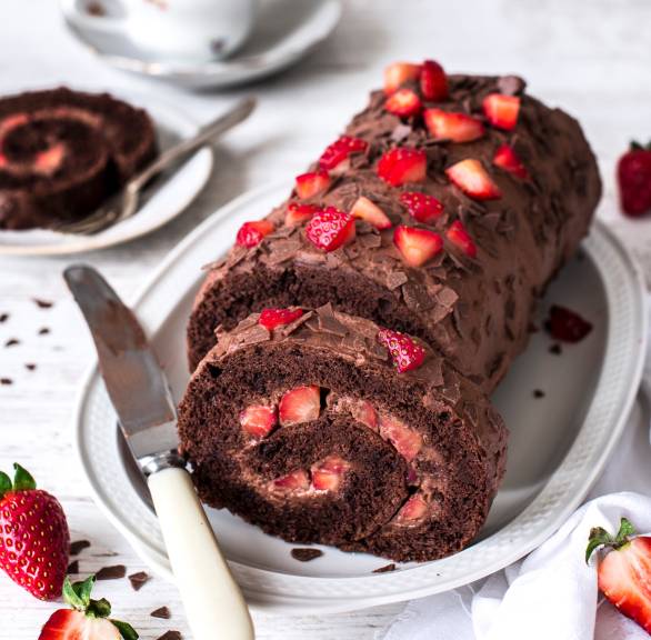 Erdbeer-Biskuitrolle aus Schokoladenbiskuit mit Schokosahne angeschnitten auf einem Kuchenteller