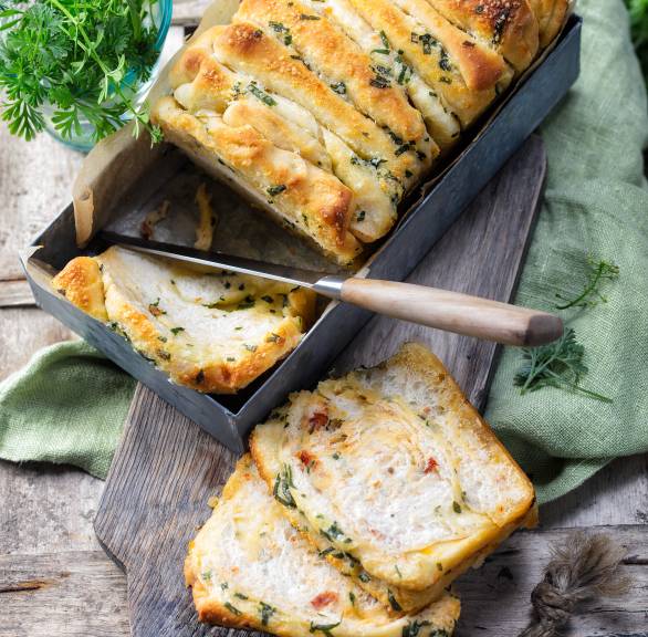 Zupfbrot mit Bärlauch-Kräuterbutter in einer Kastenform, daneben ein paar Scheiben auf einem Teller