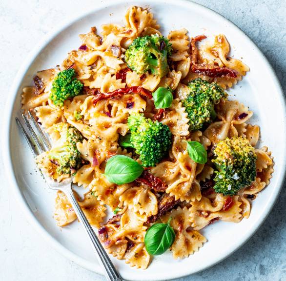 Farfalle mit Brokkoli, Pesto-Sahnesoße und getrockneten Tomaten auf einem Teller von oben