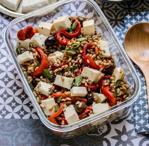 Farro-Salat mit Feta, Paprika und Oliven in einer Glasdose auf einem Tisch, daneben Olivenöl