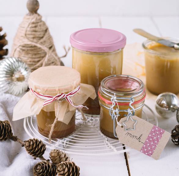 Selbst gemachte Karamellcreme in Gläser abgefüllt und als Geschenk verpackt auf einem Holztisch