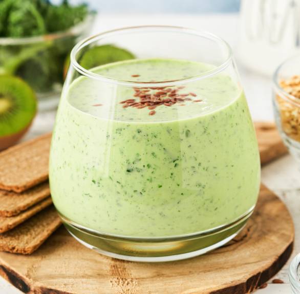 Grüner Smoothie in einem Glas, daneben Spinat, Fenchel, Kiwi und Leinsamen auf einem Tisch