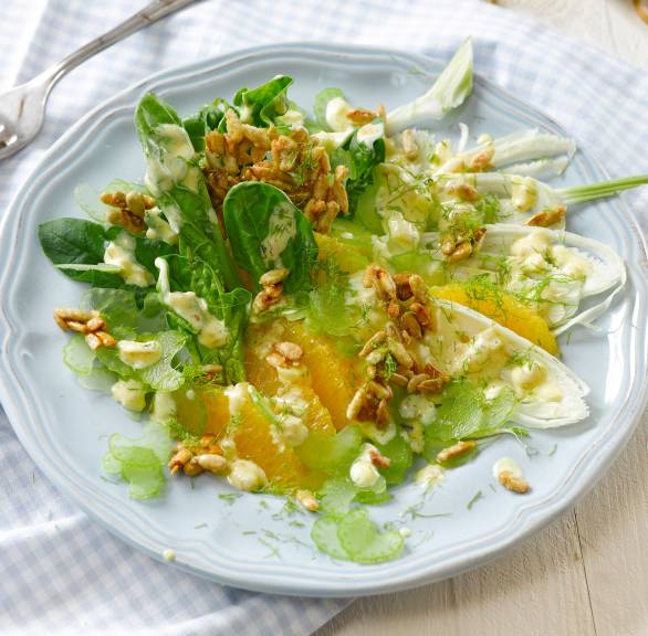 Spinat-Fenchelsalat getoppt von mit Orangen und karamellisieren Sonnenblumenkernen angerichtet auf einem Salattteller