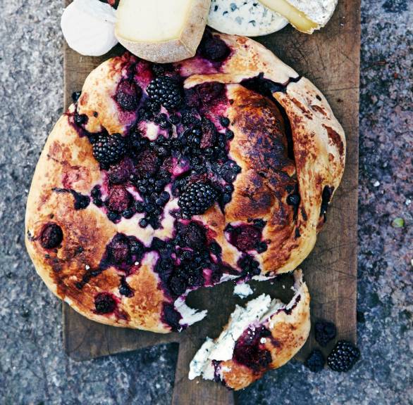 Focaccia mit Brombeeren, Blaubeeren und Rosmarin auf einem Holzbrett, daneben verschiedene Käsestücke