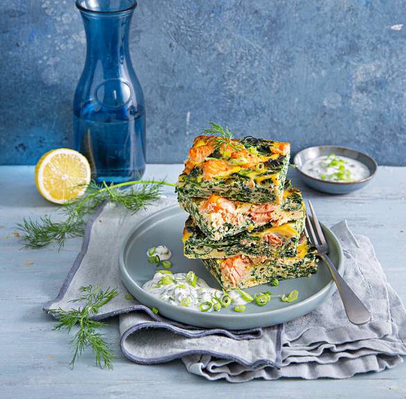 Grünkohl-Lachs-Frittata in Stücke geschnitten und gestapelt auf einem Teller, daneben Joghurt-Dill-Dip
