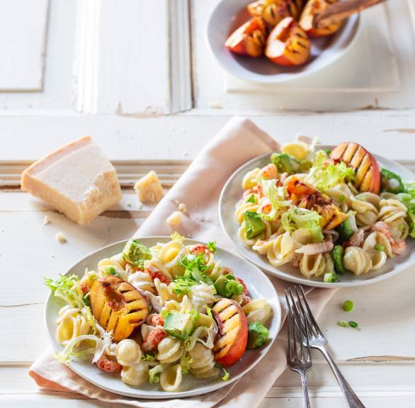 Pastasalat mit Flusskrebsfleich auf einem Teller getoppt von gegrillten Nektarinenstücken und Avocado