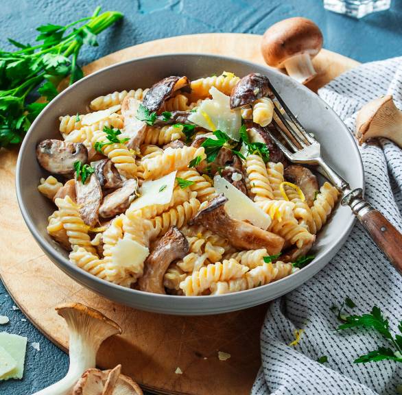 Nudeln in cremiger Mascarpone-Pilz-Sauce getoppt von Parmesan in einem tiefen Teller, daneben Pilze