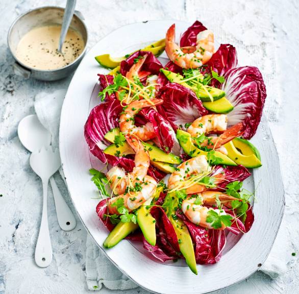 Radicchio-Avocado-Salat getoppt mit Garnelen angerichtet auf einer Servierplatte, daneben eine Schale mit Dressing