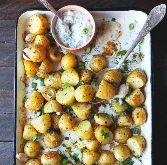 Ogengebackene Knoblauchkartoffeln auf einem Backblech, darauf eine Schale Joghurtdip