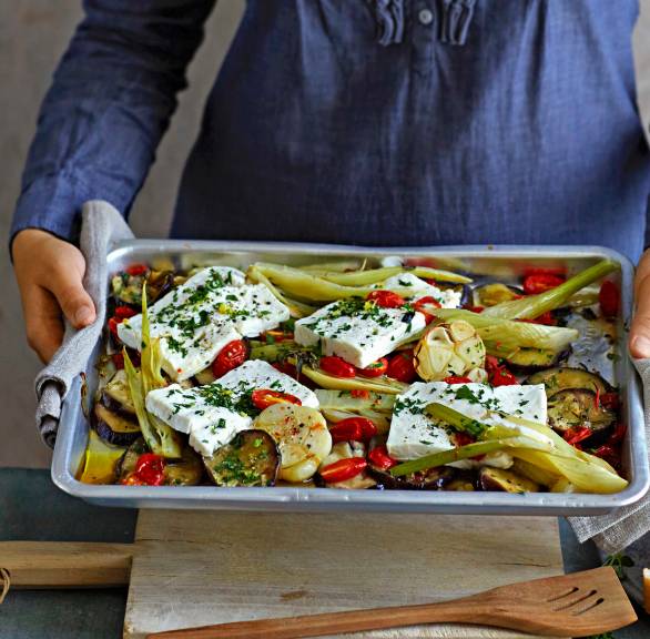 Eine Frau hält ein Backblech mit Auberginen-Fenchel-Gemüse und mit Feta