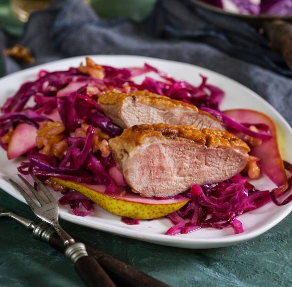 Gebratene Entenbrust in Scheiben auf einem Teller mit Birnen-Rotkohlsalat