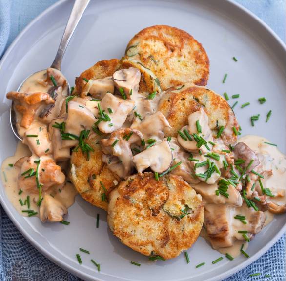 Gebratene Serviettenknödel in Scheiben angerichtet mit Pilzragout auf einem Teller