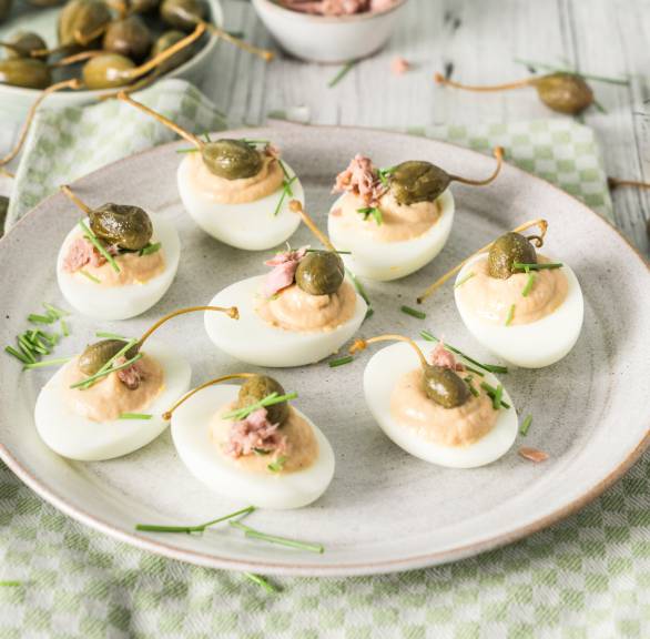 Gefüllte Eier nach Vitello-tonnato-Art auf einer Platte, daneben Kapernäpfel auf einem Tisch