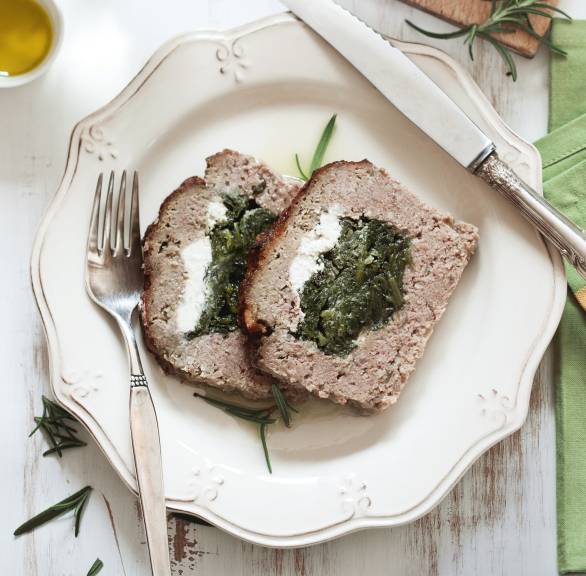 Zwei Stücke Hackbraten gefüllt mit Spinat und Ziegenkäse auf einem Teller, der kastenförmige Rest auf einem Holzbrett