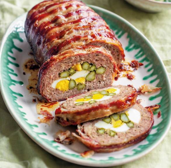 Lamm-Hackbraten im Speckmantel gefüllt mit grünem Spargel und Ei angeschnitten auf einer Servierplatte
