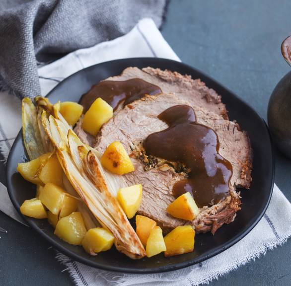 Gefüllter Rinderbraten auf einem Teller, daneben Kartoffeln und Gemüse auf einem Teller