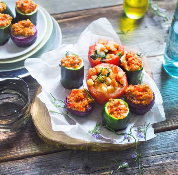 Verschiedene Gemüsestücke gefüllt mit Hirsemischung gegrillt auf einem Holzbrett, daneben Olivenöl in einer Flasche