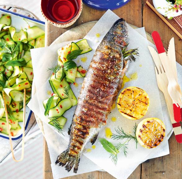 Forelle im Prosciuttomantel gegrillt auf einem Teller, daneben Zucchinisalat