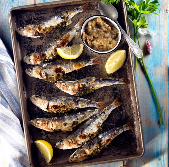 Gegrillte ganze Sardinen auf einer Platte, daneben selbst gemachte Auberginencreme in einer Schale