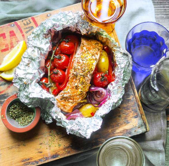 Gegrillte Lachspäckchen mit Gemüse in Alufolie auf einem Tisch