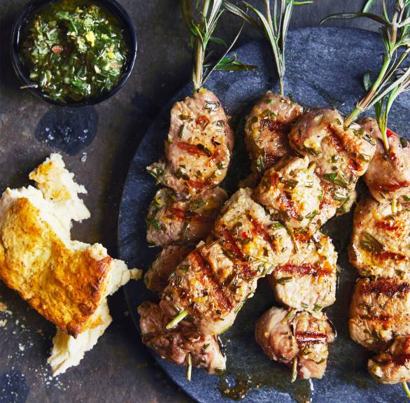 Gegrillte Lammspieße auf einem Teller, darauf kräutersoße, daneben geröstetes Brot