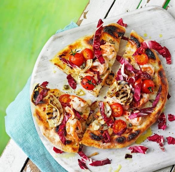 Gegrillte Pizza in Viertel geschnitten auf einem runden Holzbrett