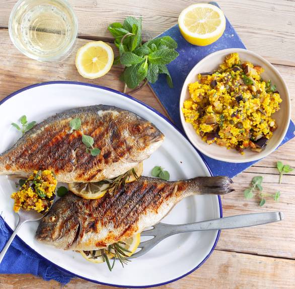 Zwei im Ganzen gegrillte Doraden auf einem Teller, daneben Couscoussalat in einer Schüssel