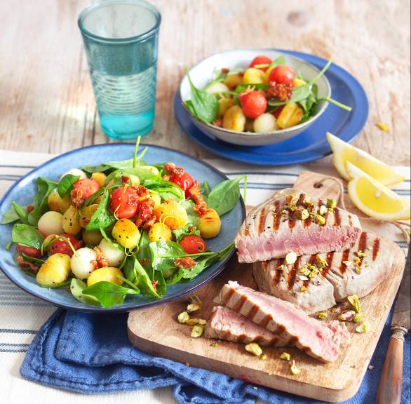 Gegrillte Thunfischsteaks in Dreiecke geschnitten auf einem Teller, daneben Salat mit Gnocchi in einer Schüssel