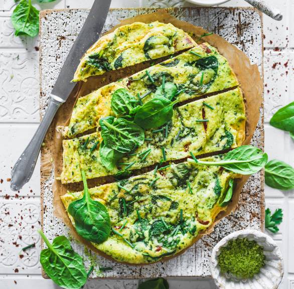  Low Carb Gemüse-Omelett mit Spinat und Parmesan in Streifen geschnitten auf einem Holzbrett, daneben Kräuterdip