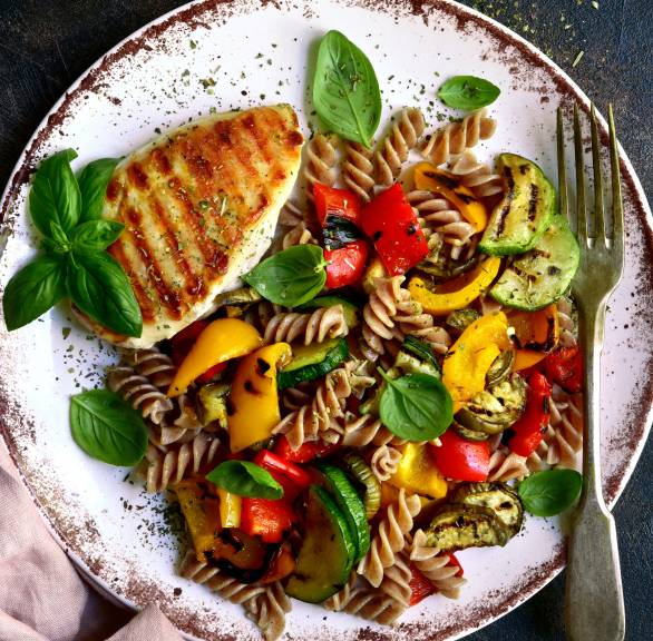 Vollkornnudeln, Gemüse und Hähnchenbrust angerichtet auf einem Teller