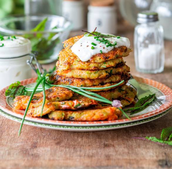 Kartoffel-Gemüse-Bratlinge gestapelt auf einem Teller getoppt mit Quark-Dip und Schnittlauch