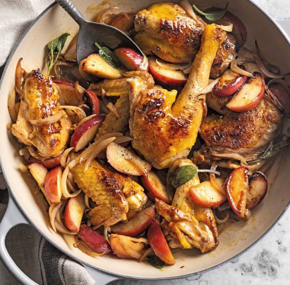 Ofenform mit geschmorten Teilen von Maishähnchen, Äpfel und Zwiebeln auf einem Tisch