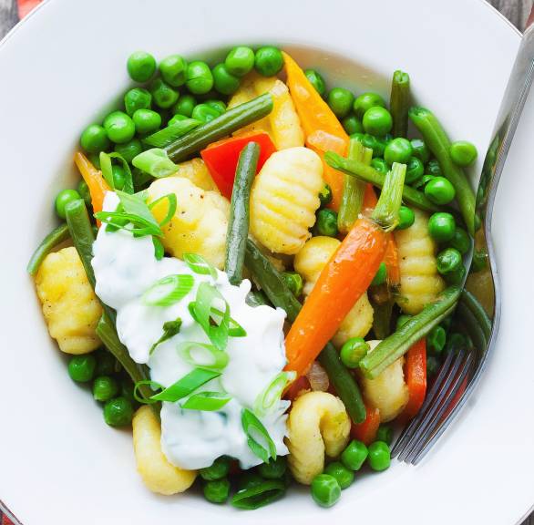 Gnocchi-Gemüse-Pfanne auf einem Teller getoppt mit Joghurt-Dip