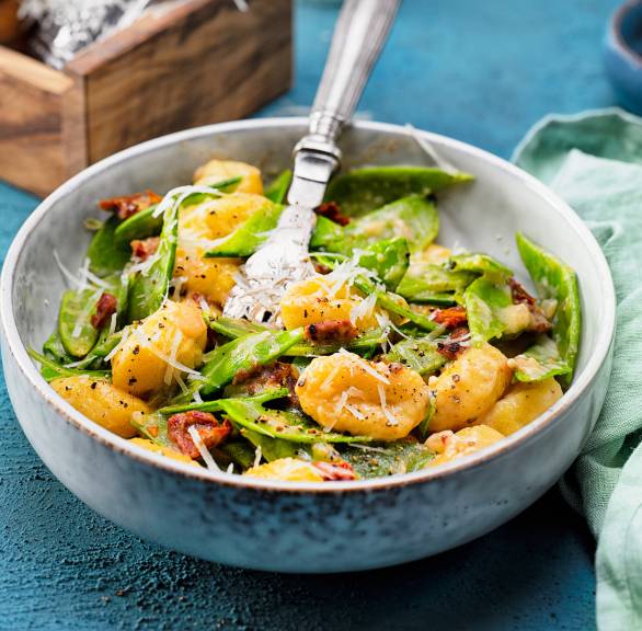 Gnocchi mit Zuckerschoten und getrockneten Tomaten in Parmesansauce angerichtet auf einem tiefen Teller