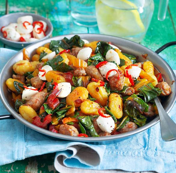 Mangold-Pfanne mit Gnocchi und Bratwurst in einer Pfanne auf einem türkisen Holztisch