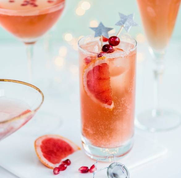 Cranberry-Tequila-Cocktail mit Prosecco garniert mit Eiswürfel und Grapefruitscheiben in Longdrinkgläsern auf einem Party-Tisch