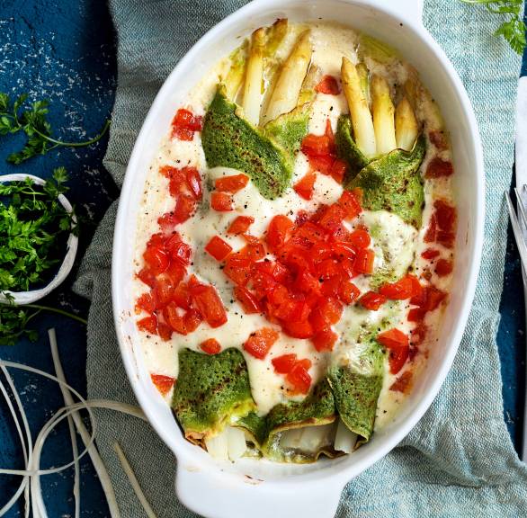 Überbackene italienische Kräuter-Crespelle mit weißem Spargel, Béchamelsoße und Tomatenwürflen in einer Auflaufform