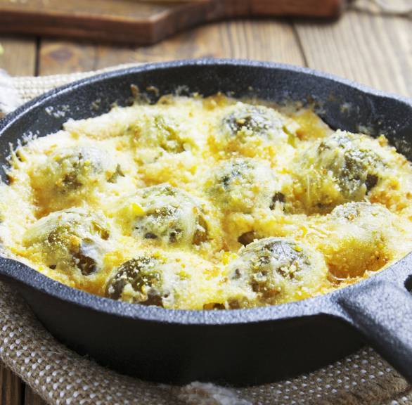 Rosenkohlgratin in einer Pfanne auf einem Tisch, daneben Parmesan am Stück