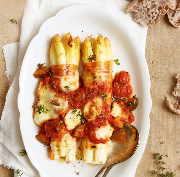Zwei Pakete überbackene Spargel-Schinken-Röllchen in Tomatensoße mit Mozzarella auf einer Servierplatte
